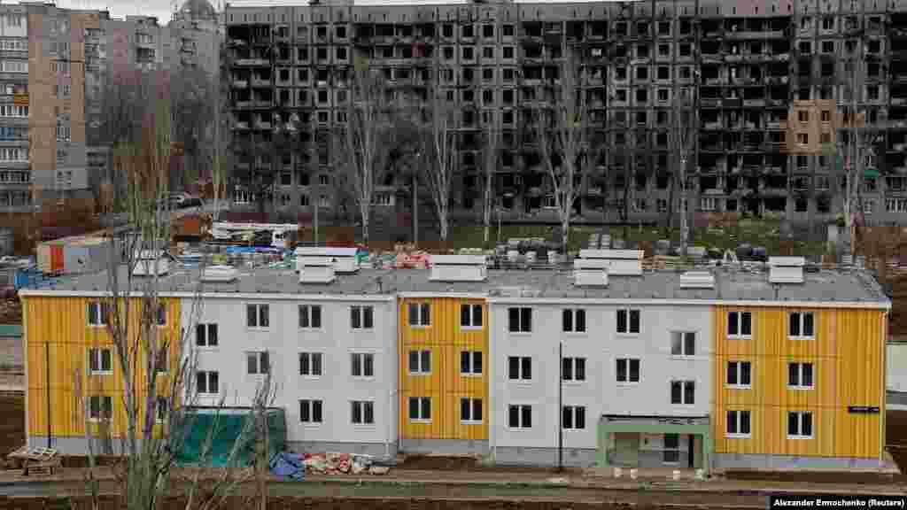 Egy új épület egy lerombolt lakóház előtt. Alekszej Navalnij ellenzéki aktivistacsoportja azt állítja, hogy magas rangú orosz tisztviselők személyesen profitálnak a Mariupolban folyó újjáépítési projektekből
