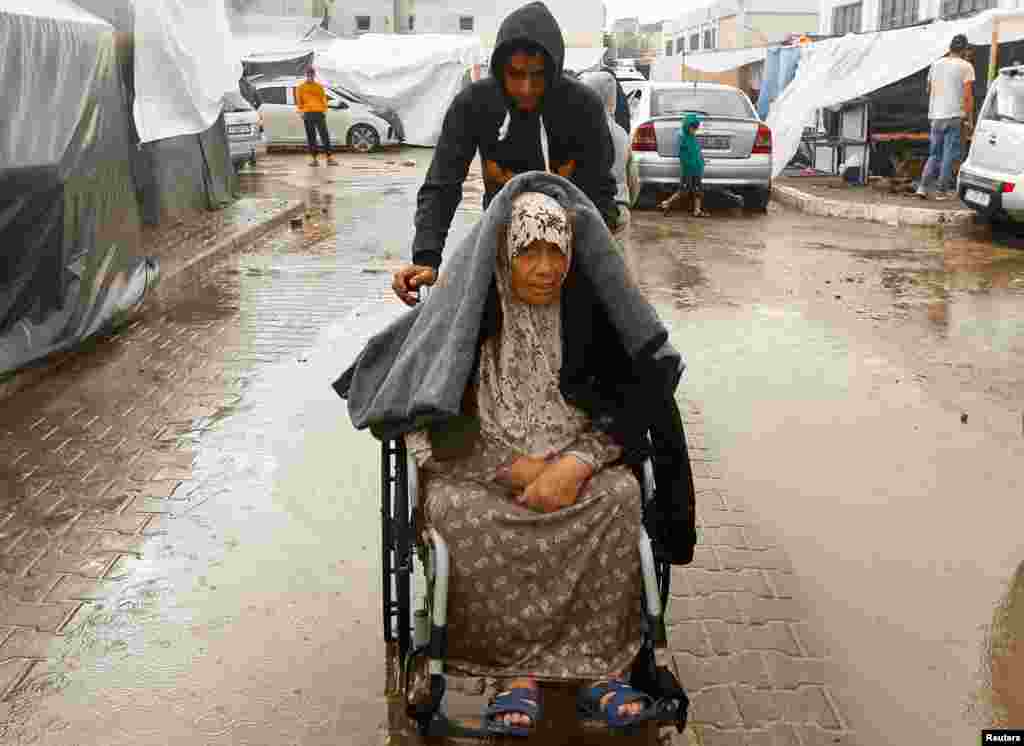 Një djalë ndihmon një grua palestineze në një karrocë me rrota në mes të shiut. 