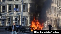 Мужчины бегут с места удара российских военных, когда горят автомобили в центре Киева, Украина. 10 октября 2022 года. 