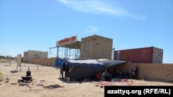 Бастующие работники на фоне вывески перед офисом предприятия. Жанаозен, 2 июня 2022 года