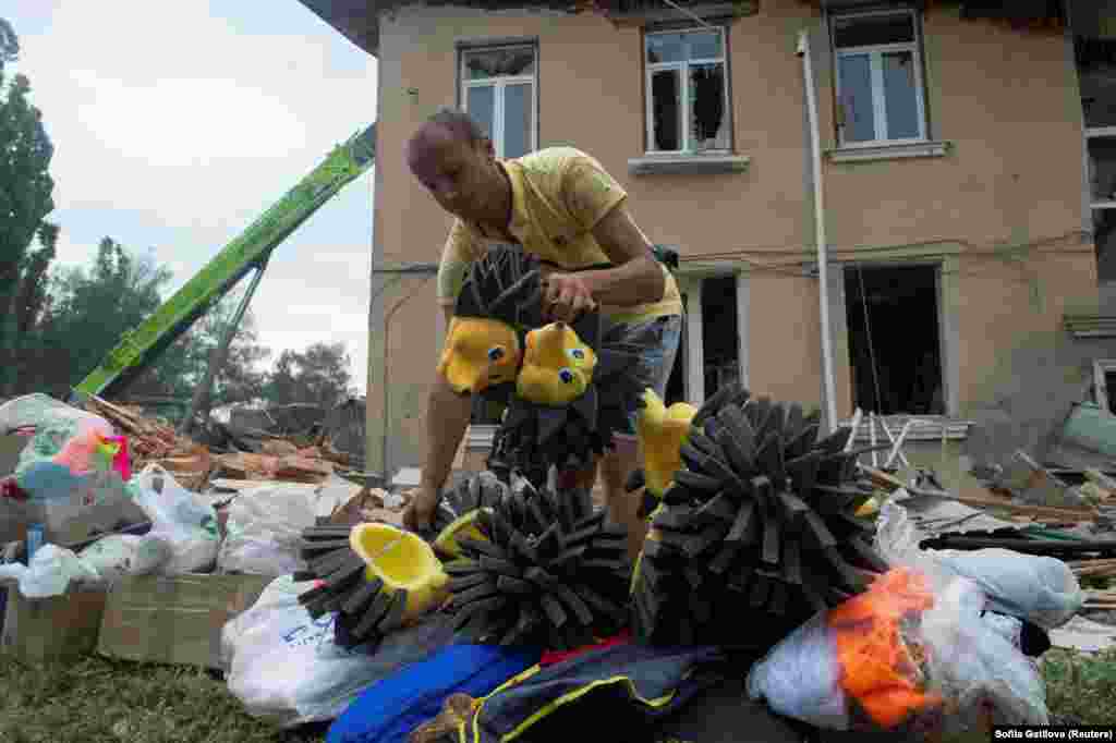 Украинанын Харьков облусундагы Чугуев шаары. Орусиянын ракеталык соккусунан талкаланган маданият үйүнүн имаратынын алдында балдардын оюнчуктарын чогултуп жаткан киши. 