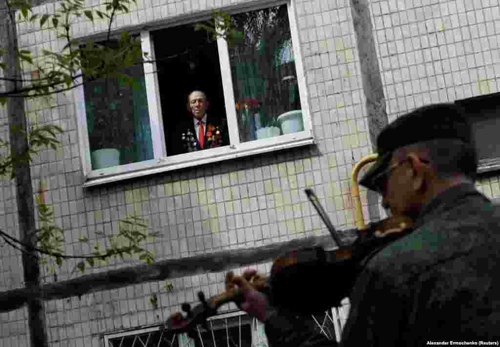 96-летний ветеран Второй мировой войны смотрит из окна своей квартиры на музыкантов, которые играют для него по случаю «Дня победы». Оккупированный Донецк, 9 мая