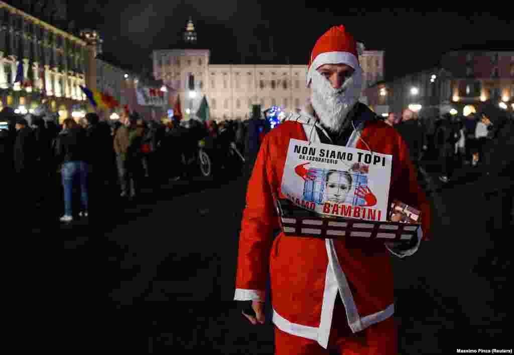 „Nem laboratóriumi egerek vagyunk, hanem gyerekek” – olvasható a Mikulásnak öltözött tüntető nyakában Torinóban december 18-án