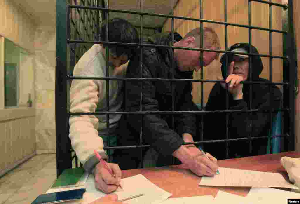 Красноярскідегі полиция бөлімінде қамауда отырған, бұрынғы совет республикаларынан шыққан заңсыз мигранттар құжатқа қол қойып жатыр. Қыркүйек, 2013 жыл.