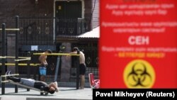 Люди на спортплощадке рядом с плакатом с информацией о профилактике COVID-19. Алматы, 12 июля 2020 года.