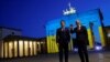 Канцлер Германии Олаф Шольц и президент Франции Эммануэль Макрон у Бранденбургских ворот в Берлине, которые подсвечены в цветах украинского флага. 9 мая 2022 года