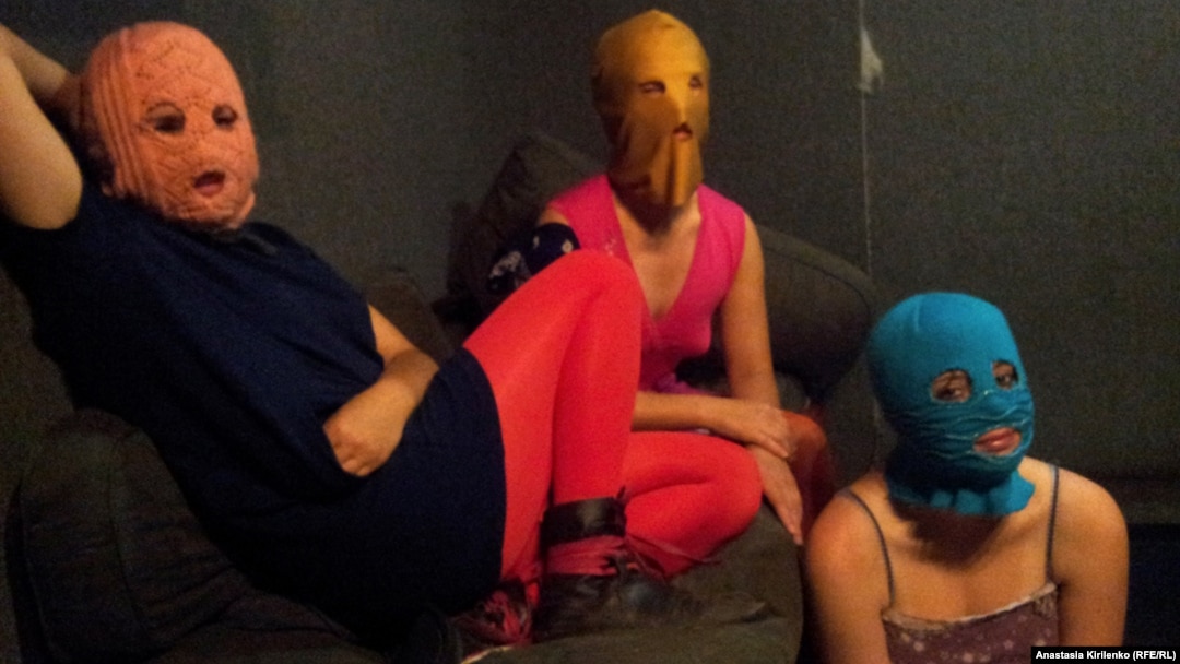 The three Pussy Riot members gathered in a darkened studio, with all three wearing the brightly colored stockings and the group's requisite balaclavas in gold, orange, and blue.