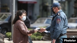 Armenia -- A police officer enforcing a coronavirus lockdown checks a woman's documents, Yerevan, March 25, 2020.