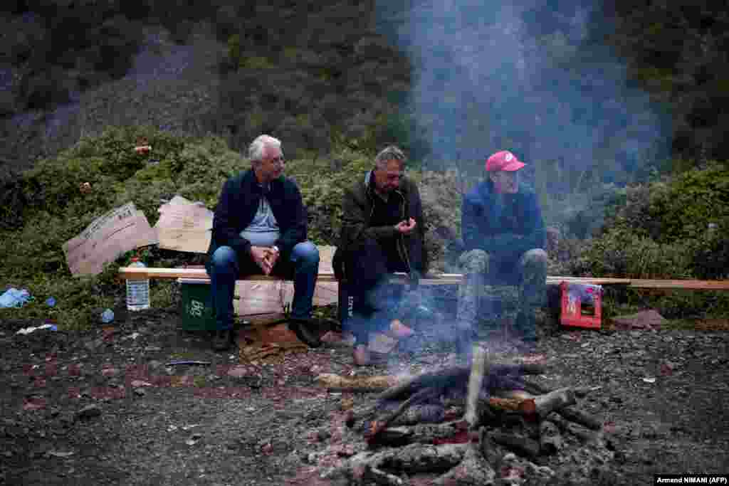 Sârbi kosovari stau lângă un foc făcut în apropierea punctului de trecere a frontierei dintre Kosovo și Serbia, în Jarinje la 28 septembrie 2021. Comunitatea internațională, condusă de Uniunea Europeană, cheamă la discuții cele două guverne, pentru a ușura tensiunile dintre Serbia și fosta sa provincie majoritară etnico-albaneză.&nbsp; Forța de menținere a păcii KFOR, condusă de NATO, a declarat că &bdquo;monitorizează îndeaproape situația din Kosovo și rămâne concentrată ... pentru a asigura un mediu sigur și libertate de circulație pentru toate comunitățile&rdquo; care trăiesc pe teritoriul separatist.
